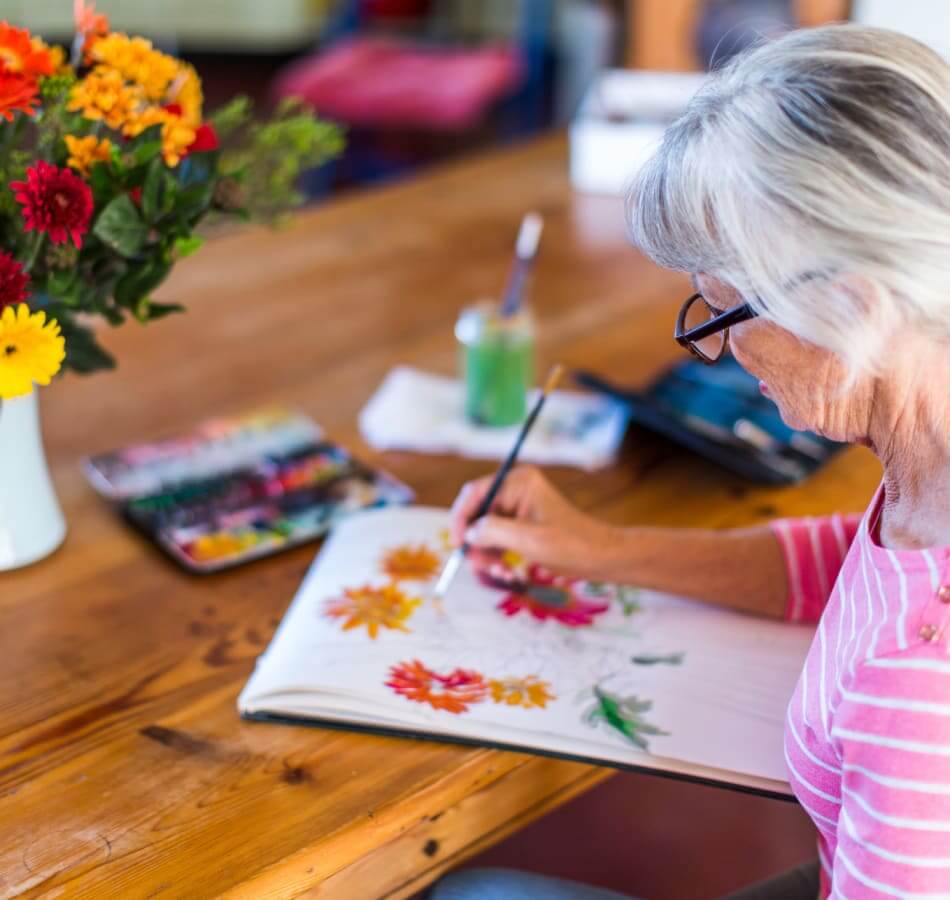 Older woman painting colorful flowers with watercolors during a creative activity at Village on the Park Bentonville, AR